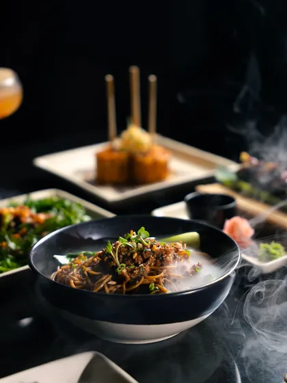 Flavours that touch the soul. A spread of our pan-Asian dishes, including steaming Dan Dan noodles, crispy corn, and fresh greens, ready to be shared.