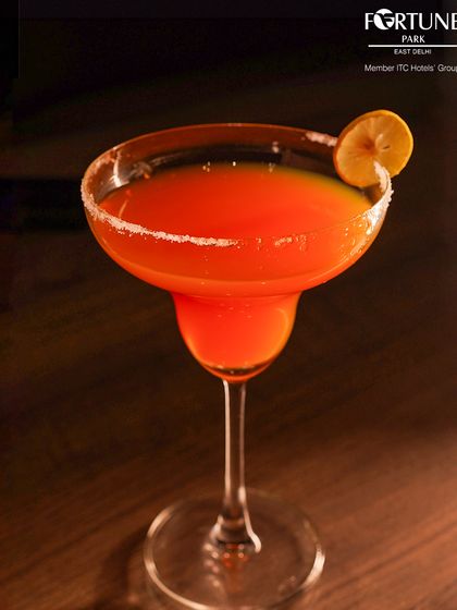 A classic margarita with a salted rim, glowing with a vibrant orange hue. It's a timeless cocktail, perfectly executed by our bartenders.