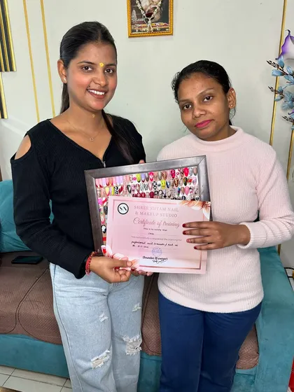 A proud moment with a graduating student, holding her certificate and the frame of diverse nail art she created.