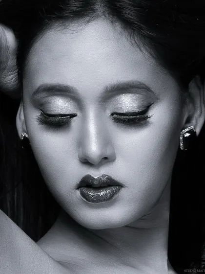 A serene black and white beauty close-up. This shot focuses on the delicate details of the makeup, from the shimmering eyeshadow to the bold lip.