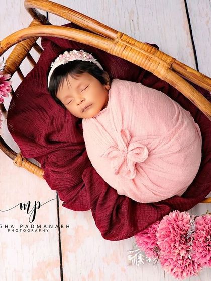 A lovely setup featuring a baby in a pink wrap, nestled in a rustic cane basket with pink and silver floral accents.