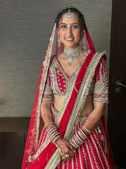 A full portrait of this happy bride. Her classic red lehenga is paired with a minimal glam look, featuring a flawless base and defined eyes, making her look timeless.