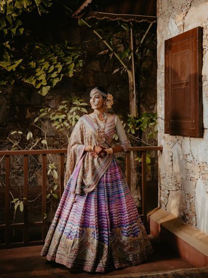 A full-length portrait of the bride in her magnificent Tarun Tahiliani lehenga. The intricate details of the outfit are beautifully captured against the rustic, natural backdrop.