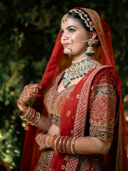 A classic three-quarter bridal portrait, capturing the bride's gentle smile and the rich details of her red wedding lehenga.