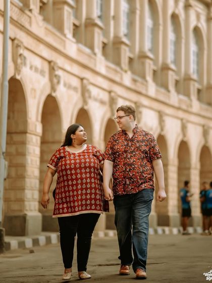 A candid moment of a multicultural couple walking hand-in-hand through the historic streets of Mumbai, showcasing a blend of love and urban charm.