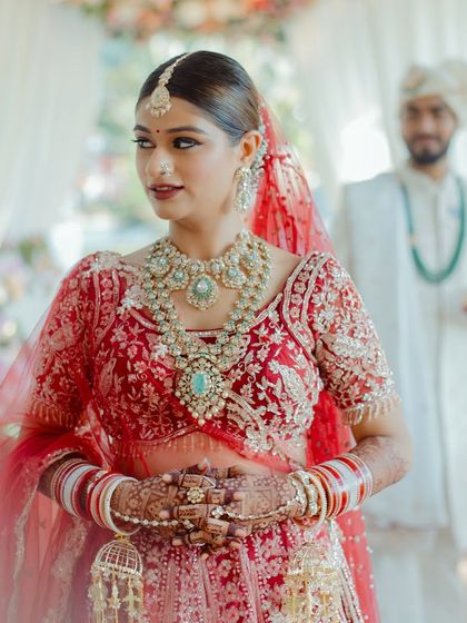 My bride Mansi, ready to walk down the aisle. Her complete look, from the intricate red lehenga to the stunning jewelry and my signature glowing makeup, creates a vision of timeless bridal elegance.