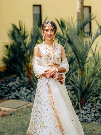 A beautiful, fresh-faced look for a Haldi ceremony. The bride wears a white lehenga with colorful embroidery, and her makeup is kept minimal and dewy to match.
