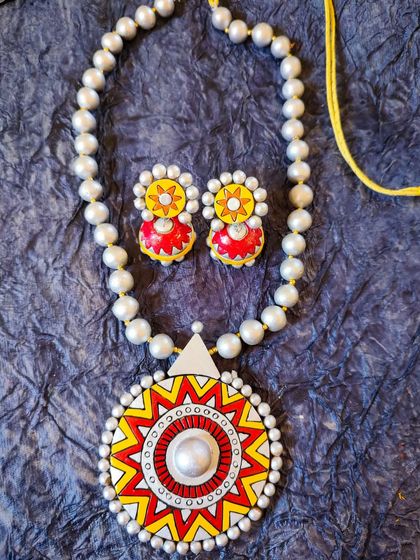 A unique terracotta set with a large, sun-like pendant in red, yellow, and white pearl. This piece is perfect for celebrating Holi or Women's Day.