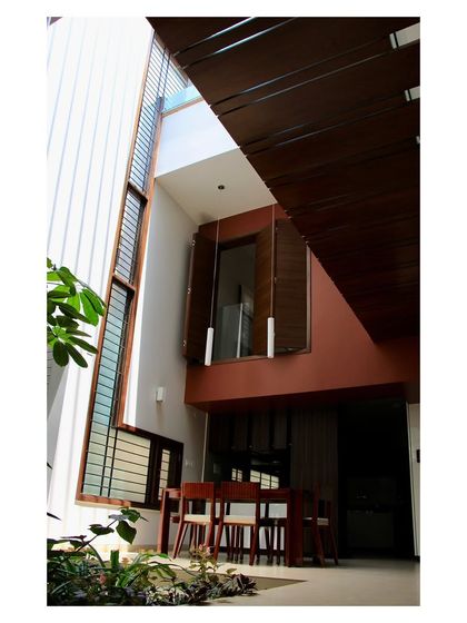 The dining area of the 'Boxed In House' is situated within the double-height courtyard space. This arrangement allows the home to breathe, creating a social hub that is visually connected to the upper floors and filled with natural light from above.