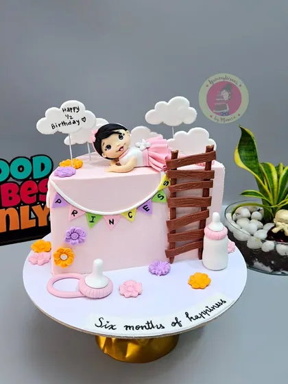 A sweet pink half-birthday cake for a little princess, featuring a baby figurine and a tiny ladder.