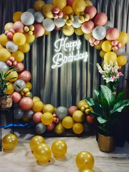An elegant birthday balloon ring set up in a living room. The gold, peach, and white balloons create a warm and inviting photo backdrop, complete with a neon sign.