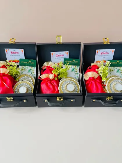 I can prepare multiple identical hampers for your corporate or family gifting needs. Here are three black suitcase boxes, each consistently packed with festive diyas, treats, and a Diwali card.