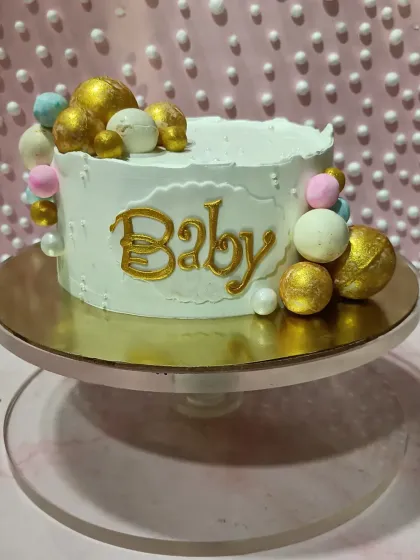 A simple and sweet "Baby" cake. The textured white buttercream is adorned with a cascade of pastel and gold chocolate spheres.