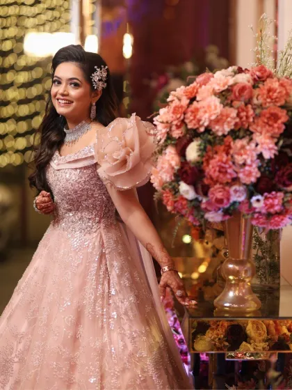 Posing by a large floral arrangement, the bride looks stunning. Her makeup is soft and elegant, complementing the romantic setting.