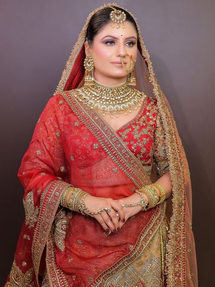 A beautiful bride in a red and gold lehenga with a sheer dupatta. This look is a testament to timeless bridal elegance, available for rent along with the jewellery.