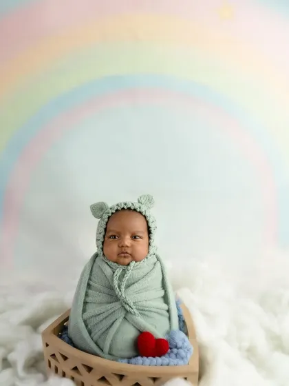 This alert baby is ready for their close-up, sitting in a basket with a cute bear-ear bonnet against a dreamy rainbow backdrop.