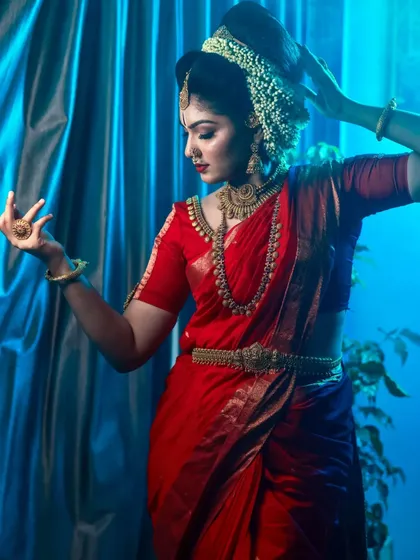 My studio work allows for complete control over lighting to create dramatic, editorial portraits. The contrast of the vibrant red saree against the cool blue backdrop, combined with precise lighting, sculpts the bride's features and highlights her graceful dance-like pose.