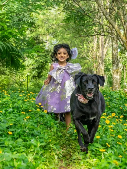 Pure, unadulterated joy. A little girl and her black Lab, Bagheera, run towards the camera through a field of green and yellow, their happiness absolutely infectious. This is the kind of energetic, candid moment I love to capture.