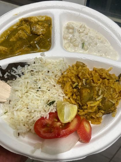 A party plate filled with our delicious food. This meal includes biryani, jeera rice, a chicken curry, raita, and salad, showing the variety we can offer for bulk orders.