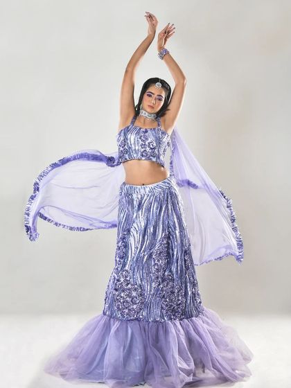 A full-length shot of a model in a sparkling lavender lehenga, perfect for an engagement or sangeet. The makeup is glamorous with a defined eye and a soft lip color to match the outfit.
