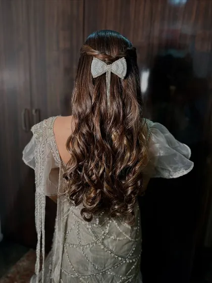 A cute and modern half-up hairstyle featuring soft waves and a sparkling bow accessory. Ideal for a reception or cocktail party.