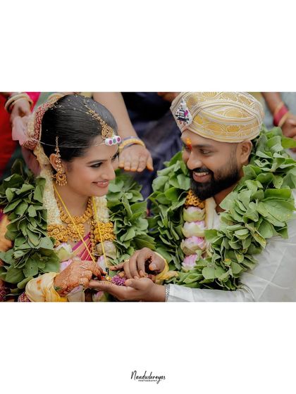 The couple shares a moment of connection during a traditional South Indian wedding ritual. The vibrant green garlands frame their happy faces perfectly.