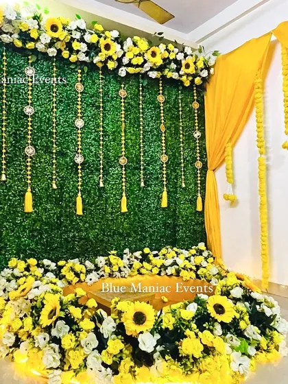 A grand Haldi setup with a green wall, yellow drapes, and a floor seating area surrounded by sunflowers. This design is perfect for making a statement.