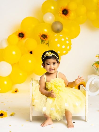 A bright and cheerful sunflower-themed first birthday shoot. The vibrant yellow balloons and flowers create a sunny backdrop for this little girl as she sits by the "One" sign.