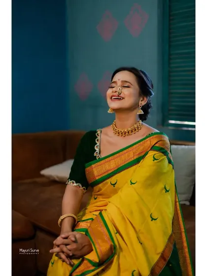 A candid moment of laughter from a studio shoot. The model, dressed in a vibrant yellow and green traditional saree, shares a genuine smile, creating a warm and inviting portrait.