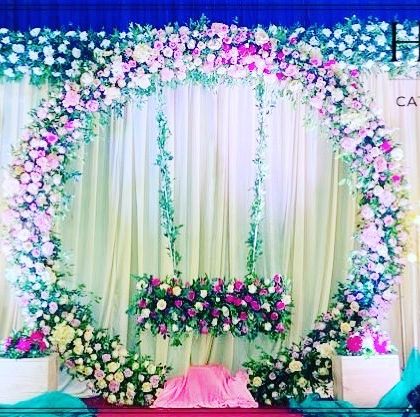 An elaborate stage for a naming ceremony featuring a large floral ring on a greenery wall. The setup is lit with candle-like floor lamps, creating a magical ambiance.