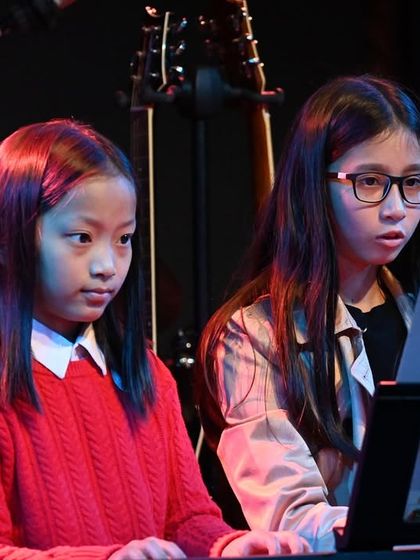A close-up of two young pianists in an ensemble, learning to read music and play together.