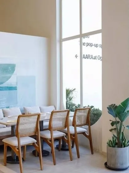 This bright and airy cafe space features my cane and wood chairs paired with a comfortable upholstered bench. The light wood finish and neutral fabrics contribute to the minimalist and modern aesthetic.