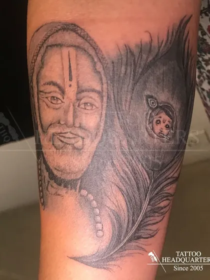 A spiritual portrait tattoo combining the face of a sage with a peacock feather that holds a tiny image of Krishna.