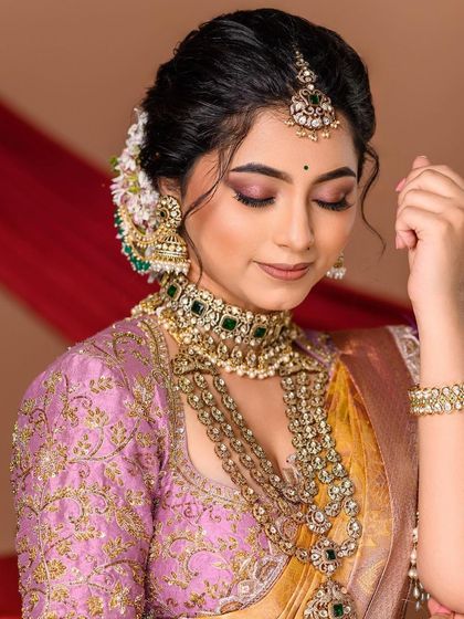 A serene moment captured. The soft lighting complements the bride's gentle expression, drawing attention to the emerald-studded choker and the delicate floral arrangement in her hair.