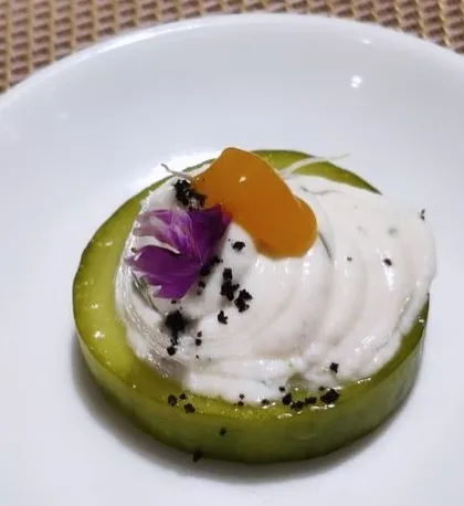 A modern canapé inspired by Indian flavors. A slice of cucumber topped with a spiced yogurt mousse and a mango pickle drop, showcasing our creative approach to hors d'oeuvres.