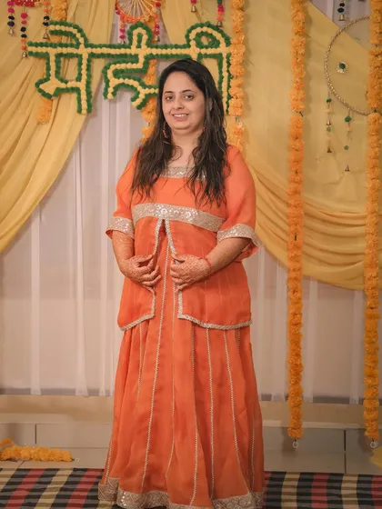 The bride posing in her orange Mehandi outfit against the festive yellow backdrop.
