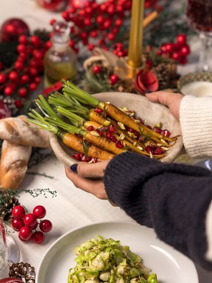 A guest passes a bowl of our honey-glazed carrots with pomegranate and pistachios. Our side dishes are crafted to be as memorable as the mains.