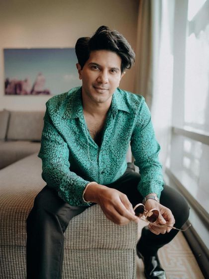 Dulquer holding his sunglasses, a key accessory that adds a touch of movie-star cool to any outfit.