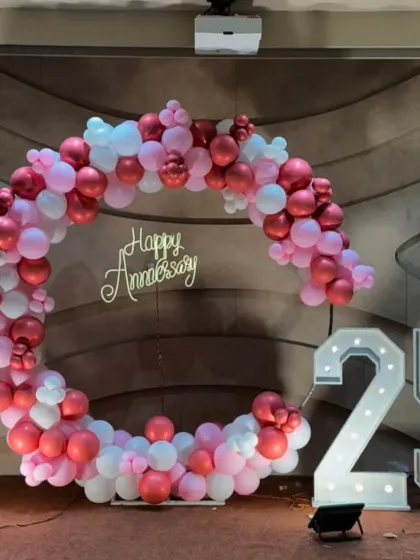 A circular balloon arch in shades of pink and white for a 25th-anniversary party, complete with marquee numbers.