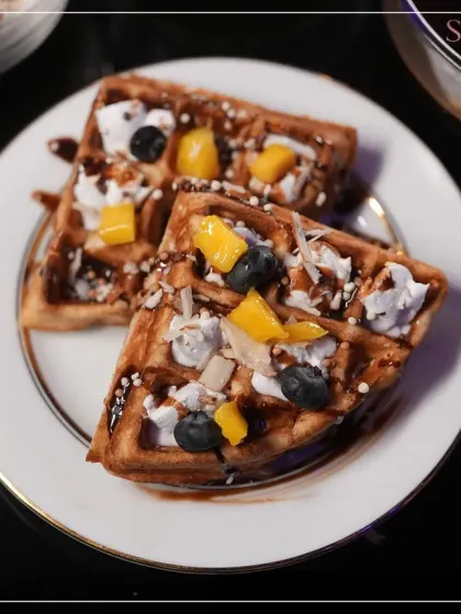 Freshly made waffles topped with mango, blueberries, and a drizzle of chocolate sauce. A delightful and indulgent dessert option for any celebration.