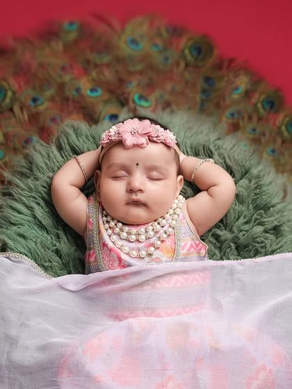 A beautiful close-up on the face of the sleeping 'Little Radha', highlighting her delicate features and the pearl necklace against the backdrop of peacock feathers.
