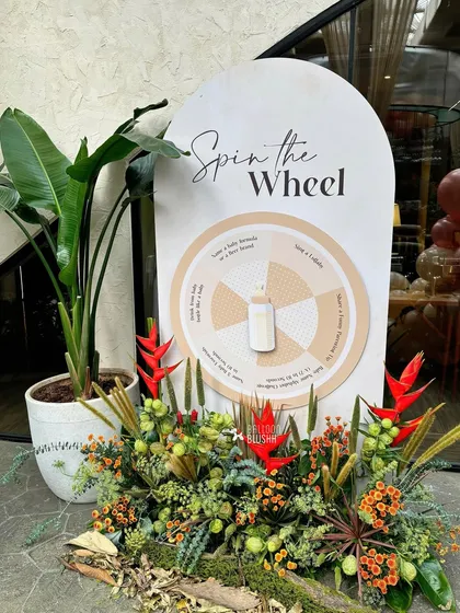 An interactive 'Spin the Wheel' game for baby shower guests, surrounded by tropical and woodland foliage.