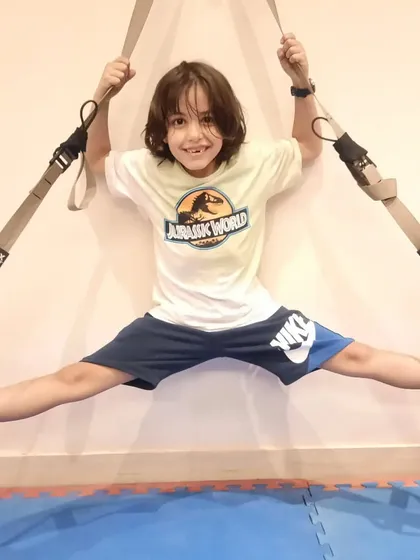 Every child can improve their flexibility with the right guidance. This young student is smiling while working on his wall split with suspension straps, showing that hard work can also be enjoyable.