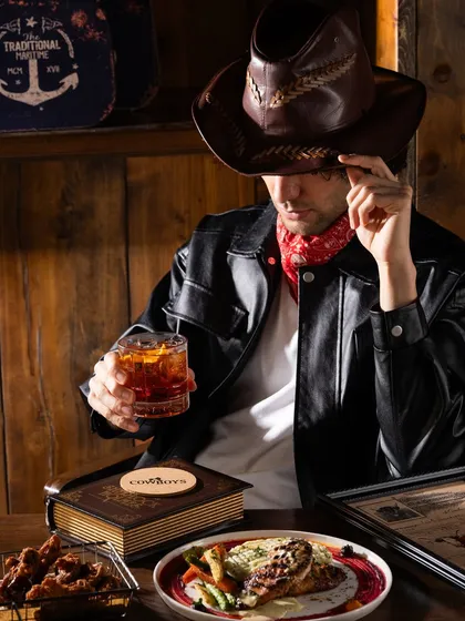 A wider shot of a model in a cowboy-themed sports bar. This image sells not just the drink, but the entire experience and atmosphere.
