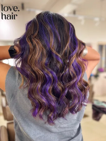 It's giving toffee crunch with a hint of blackcurrant cream. We combined a warm brown balayage with pops of vivid purple for a unique and eye-catching look.