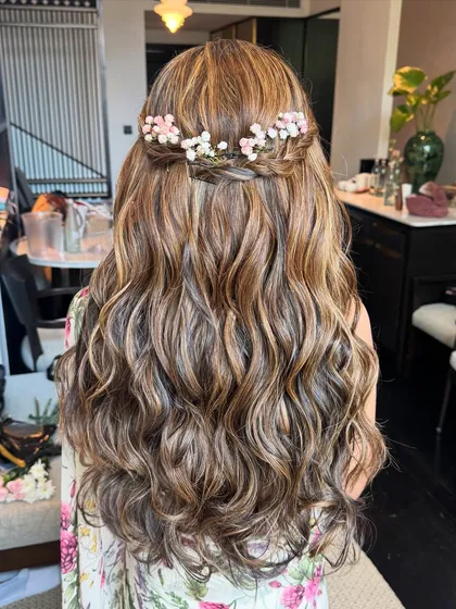A romantic half-up, half-down style with a braided crown. Tiny pink and white flowers are woven into the braid, adding a delicate and whimsical touch.