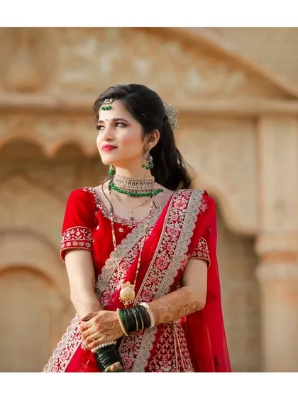 A beautiful portrait of the bride in her red lehenga, looking away thoughtfully. The soft, natural light enhances her features and the details of her attire.