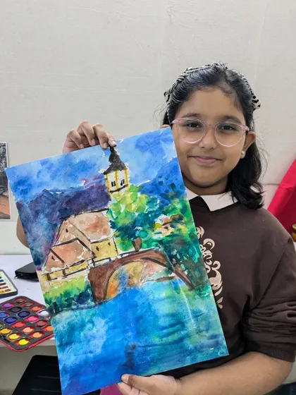 This student proudly displays her vibrant watercolor landscape of a European town, showcasing her use of bold colors and expressive brushstrokes.
