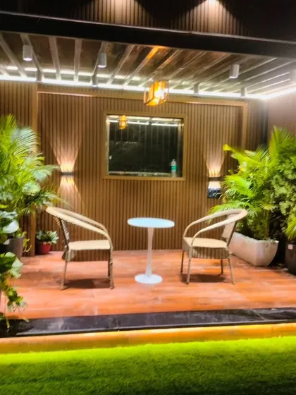 A cozy seating nook under a pergola in the Model Town project, surrounded by lush plants and warm wall-mounted lights.