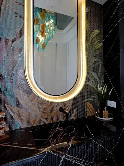 The backlit oval mirror with a gold frame beautifully reflects the chandelier, adding to the room's luxurious and glamorous feel.
